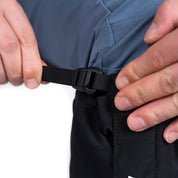 Hände ziehen an einem schwarzen Riemen, um Gamaschen 3 Lagen zum Wandern am Bund einer Hose zu fixieren. Ideal für Outdoor-Schutz.