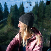 Junge Frau im Gondelwagen trägt Merino Mütze Herren & Damen Strick 230g/m2 aus 100% Merinowolle, lächelt und genießt die Bergsicht.