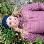 Person in mauver Jacke und Stirnband liegt lächelnd im Freien, trägt Merino Halstuch Herren & Damen, ideal für Outdoor-Aktivitäten bei kühlem Wetter, aus atmungsaktiver Merinowolle.