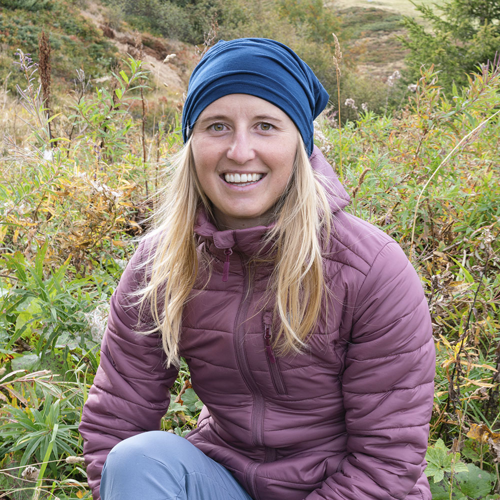 Junge Frau in lila-mauver Jacke trägt Merino Halstuch Herren & Damen, ideal für Outdoor-Aktivitäten. Atmungsaktiv und temperaturregulierend, perfekt für kühle Bedingungen.