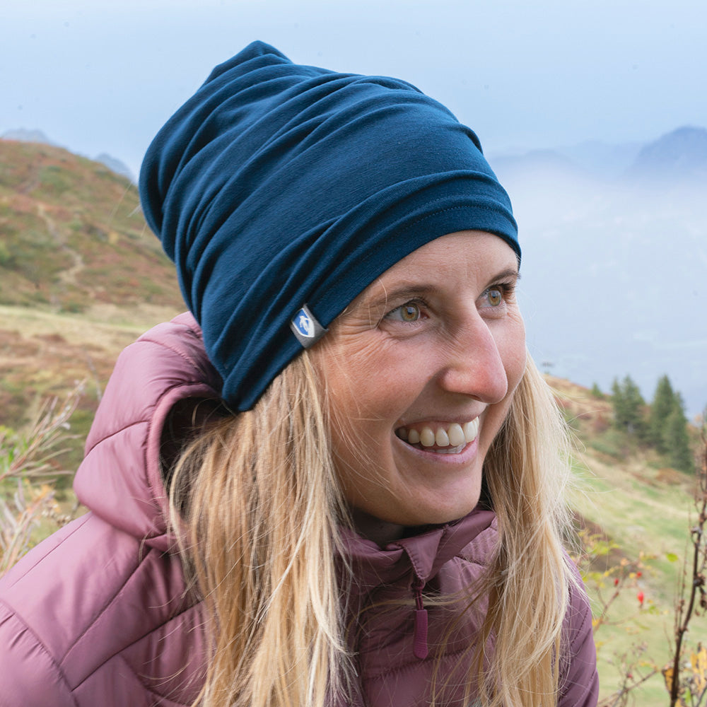 Frau auf einem nebligen Hügel trägt Merino Halstuch Herren & Damen, ideal für Outdoor-Aktivitäten. Kombiniert Merino-Komfort mit synthetischer Robustheit, perfekt für kühle Bedingungen.