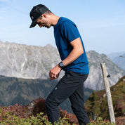 Mann in 100% Merino T-Shirt Herren 180 g/m2 wandert über steinigen Hang, ideal für Outdoor-Aktivitäten, symbolisiert Komfort und Funktionalität von alpinloacker.com.