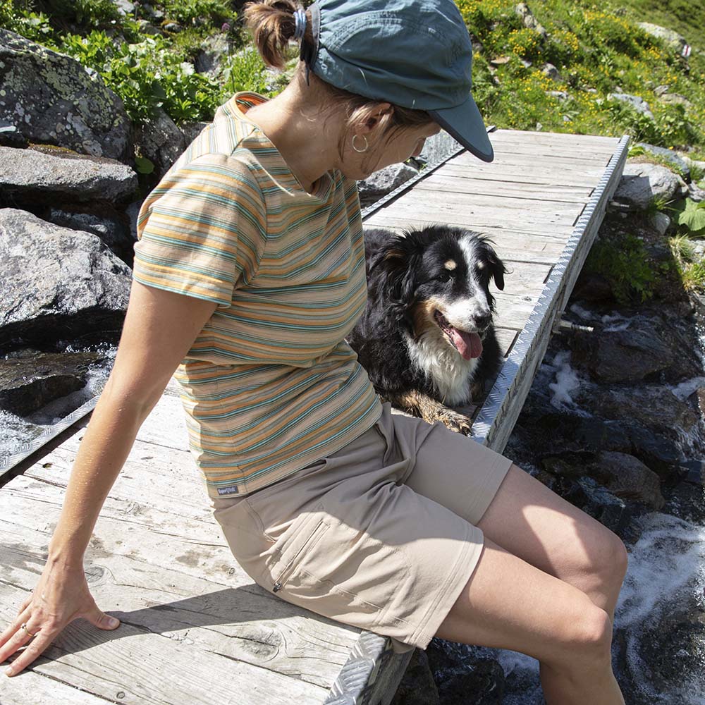 Person sitzt auf Brücke, trägt Kurze Wanderhose Damen. Neben ihnen ein zufriedener Hund. Hose bietet Komfort und Funktionalität für Outdoor-Abenteuer.