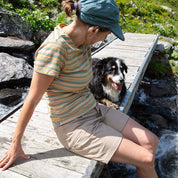 Person sitzt auf Brücke, trägt Kurze Wanderhose Damen. Neben ihnen ein zufriedener Hund. Hose bietet Komfort und Funktionalität für Outdoor-Abenteuer.