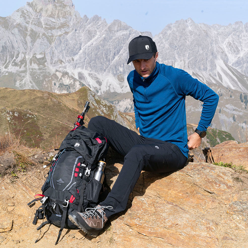 m², sitzt mit Rucksack auf Felsen in bergiger Landschaft. Ideal für Outdoor-Aktivitäten.