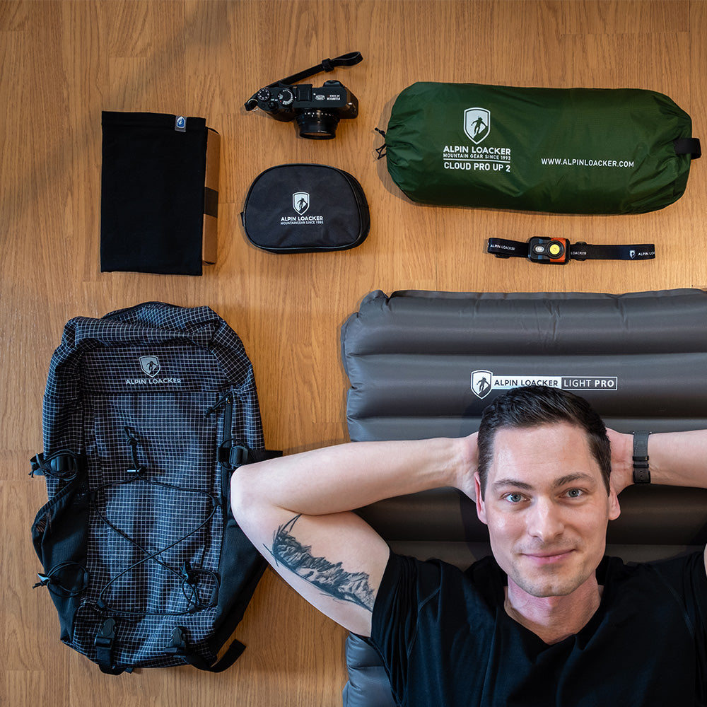 Mann auf Light Pro Isomatte, umgeben von Alpin Loacker Campingausrüstung, darunter der leichte 30L Allround Rucksack für Wandern & Reisen mit Dyneema Ripstop-Nylon.