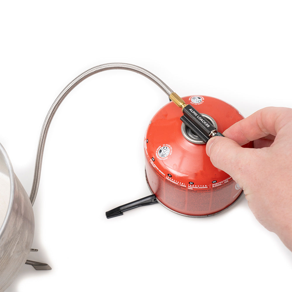 Hand befestigt Adapter am roten Isobutan/Propan-Kanister mit flexiblem Schlauch, passend für den leichten stabilen Performance Gaskocher aus Titan 128g von Alpin Loacker.