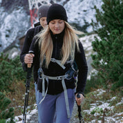 Zwei Wanderer in Outdoor-Bekleidung, vorne Frau mit Alpin Loacker Merino Jacke Damen 270 g/m², nutzen Trekkingstöcke auf verschneitem Bergpfad.