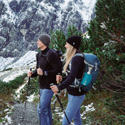 Zwei Wanderer in Merino Jacke Herren 270 g/m² auf Bergpfad, ausgestattet für kühles Wetter mit Rucksäcken und Stöcken, vor schneebedeckter Bergkulisse.