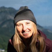 Junge Frau mit Merino Mütze Herren & Damen Strick 230g/m2 auf Bergwanderung, lächelnd. Beanie aus 100% Merinowolle, ideal für Outdoor-Aktivitäten.