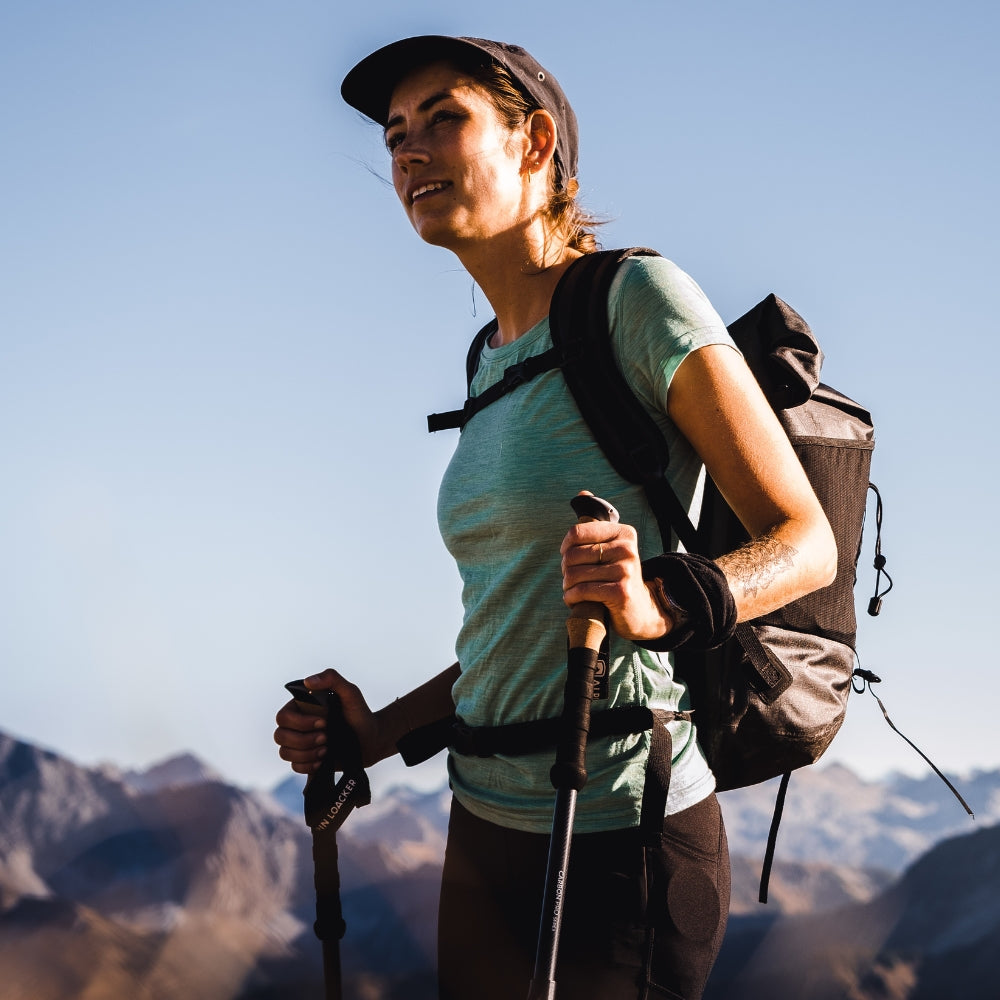Hiker in den Bergen trägt das Merino T-Shirt Damen 150g/m2, ideal für Outdoor-Aktivitäten durch Merinowolle und synthetische Fasern, mit Trekkingstöcken ausgestattet.