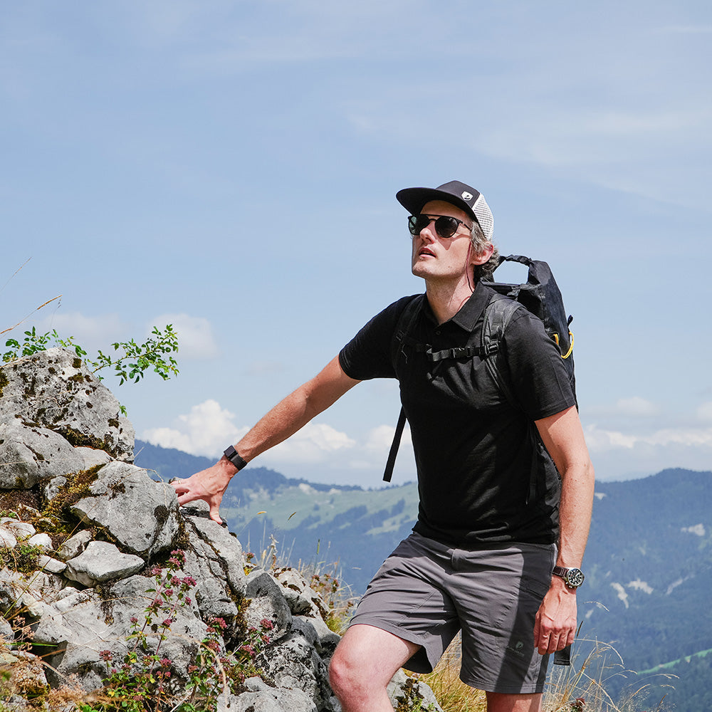 Mann steigt felsigen Hang hinauf, trägt Merino Polo Shirt Herren, ideal für Outdoor-Aktivitäten; atmungsaktiv, temperaturregulierend, geruchsresistent, nachhaltig.