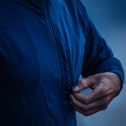 Person öffnet vertikale Tasche einer blauen Merino Jacke Herren 270 g/m², ideal für Outdoor-Abenteuer und Alltag durch Wärme, Atmungsaktivität und Flexibilität.