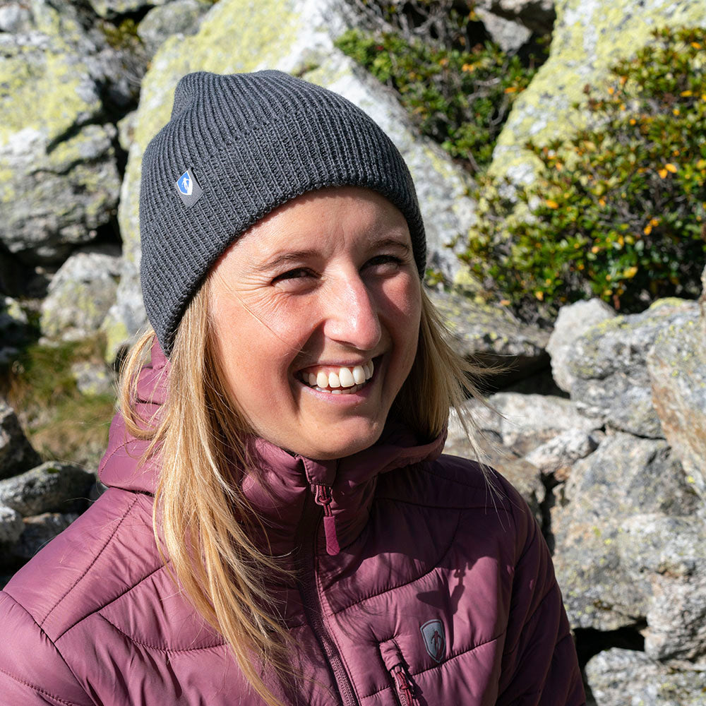 Person trägt Merino Mütze Herren & Damen Strick 230g/m² in alpiner Umgebung, passend für Outdoor-Abenteuer mit Sonnenschutz und temperaturregulierenden Eigenschaften.