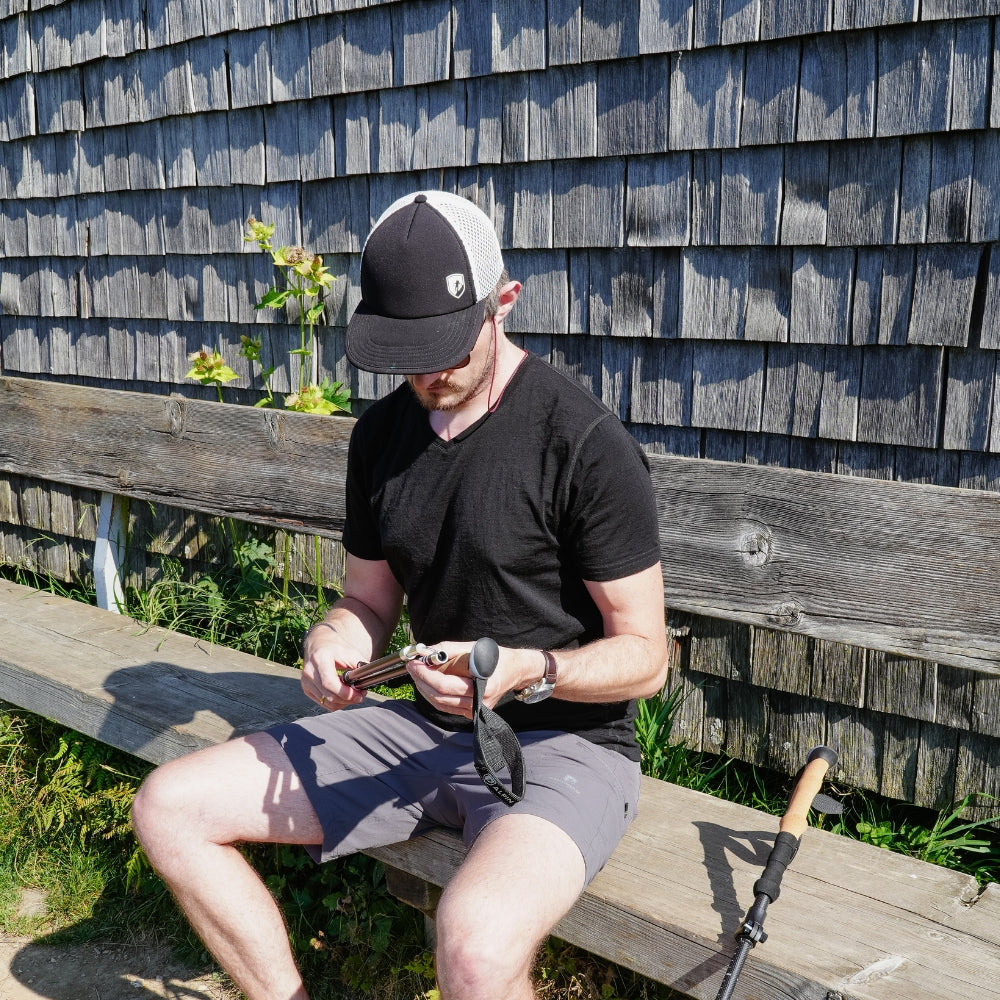 Mann sitzt auf einer Bank und hält einen Trekkingstock, trägt das Merino V-Neck T-Shirt Herren, ideal für stilbewusste Outdoor-Enthusiasten.