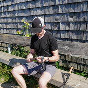Mann sitzt auf einer Bank und hält einen Trekkingstock, trägt das Merino V-Neck T-Shirt Herren, ideal für stilbewusste Outdoor-Enthusiasten.