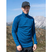 Mann in alpiner Landschaft trägt das Merino Langarmshirt mit Zip Herren 230 g/m², ideal für Outdoor-Aktivitäten, aus 100% Merinowolle für Komfort und Funktionalität.