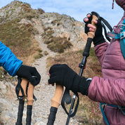 Wanderer mit Merino Handschuhe Damen & Herren, Classic und fingerlos, auf steinigem Bergpfad, halten Trekkingstöcke. Perfekt für Outdoor-Abenteuer, bieten Wärme und Geschicklichkeit.
