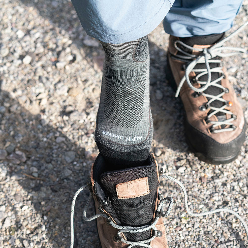 Leichte Merino Wandersocken Herren & Damen, sichtbar im unlaced braunen Wanderschuh auf Schotter, bieten Komfort für Outdoor-Aktivitäten mit atmungsaktiver, temperaturregulierender Merinowolle.