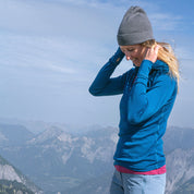 Frau trägt das Merino Langarmshirt mit Zip Damen 230g/m2 auf einem Bergkamm, ideal für Outdoor-Aktivitäten, aus atmungsaktiver, geruchsresistenter Merinowolle.