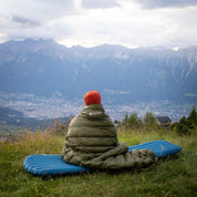 Person auf blauer Ultra Leichte Isomatte für 3 Jahreszeiten, genießt Aussicht im alpinen Gelände. Ideal für Trekking, kompakt, leicht und isoliert bis -5 °C.