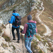 Zwei Wanderer mit dem 35-Liter-Wanderrucksack von Alpin Loacker auf einem steinigen Bergpfad, ausgestattet mit Trekkingstöcken und wetterfester Outdoor-Ausrüstung.
