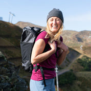 Frau trägt den leichten, wasserdichten Rucksack Lotus 25 2.0 auf einem Bergweg, ideal für Outdoor-Abenteuer.