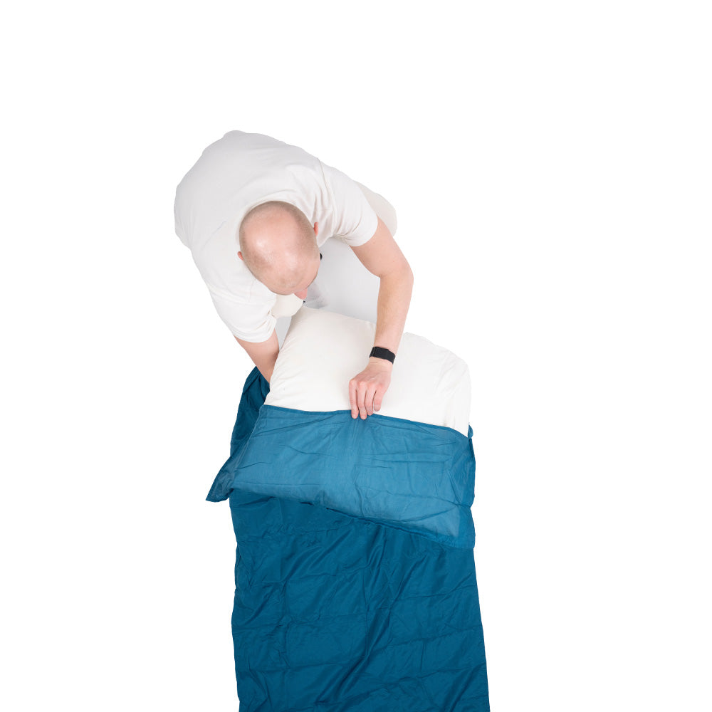 Mann legt Kissen in blauen Ultraleichter Seiden Mix Reiseschlafsack und Hüttenschlafsack, ideal für Outdoor-Abenteuer, ein.