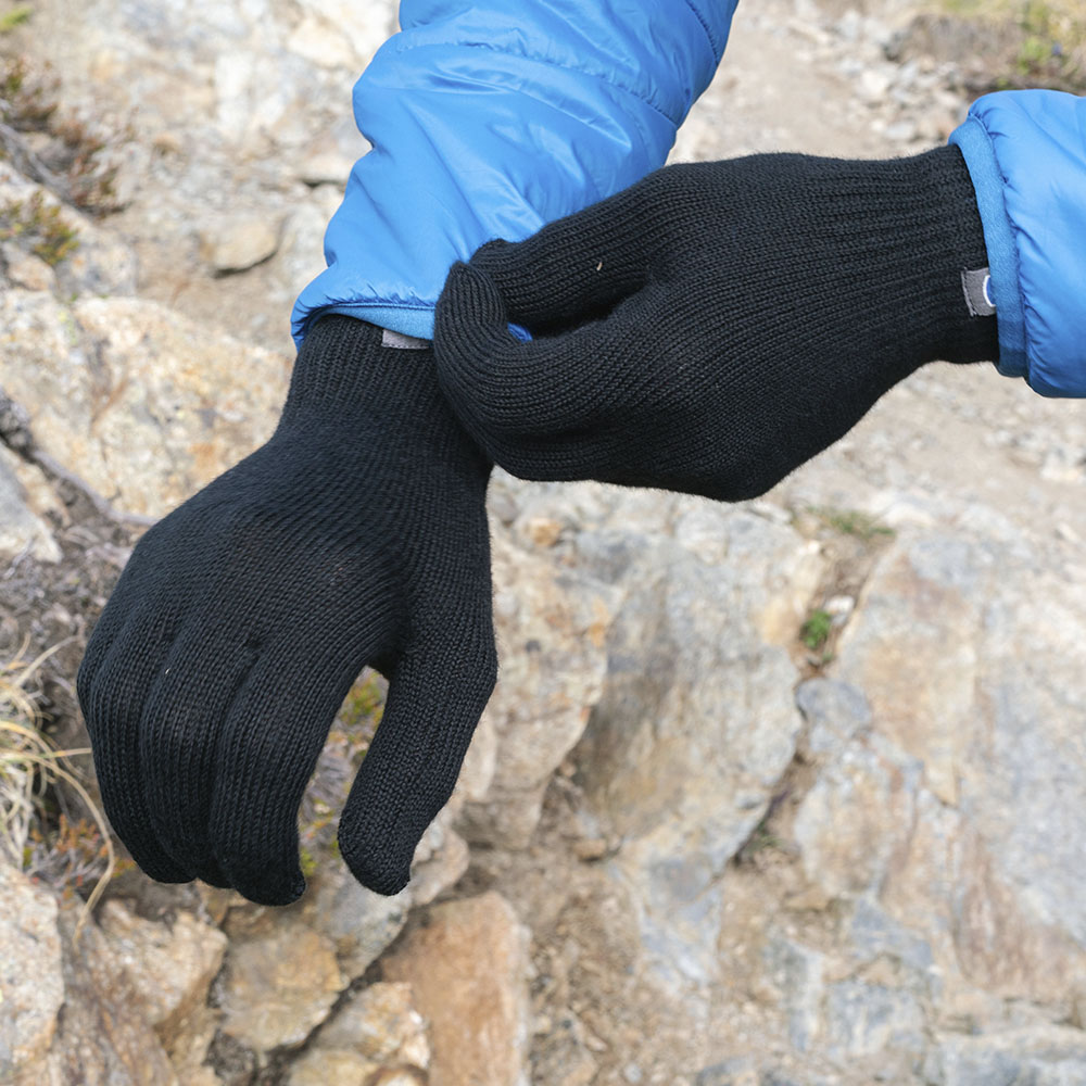 Person passt Merino Handschuhe Damen & Herren an; schwarze, gestrickte Handschuhe mit blauen Jackenärmel, ideal für Outdoor-Abenteuer und täglichen Komfort.