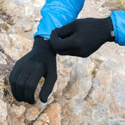 Person passt Merino Handschuhe Damen & Herren an; schwarze, gestrickte Handschuhe mit blauen Jackenärmel, ideal für Outdoor-Abenteuer und täglichen Komfort.