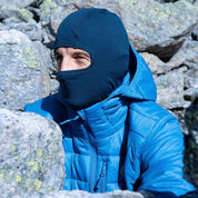 Person im Freien mit blauer Merino Sturmhaube und Skimaske Herren & Damen, ideal für kalte Outdoor-Abenteuer, trägt Alpin-Loacker-Ausrüstung in bergigem Gelände.