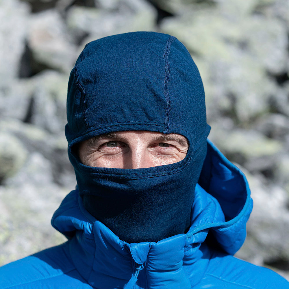Person trägt Merino Sturmhaube und Skimaske Herren & Damen in alpiner Umgebung, zeigt ergonomische Passform und Wärmeisolierung ideal für Outdoor-Aktivitäten bei kaltem Wetter.