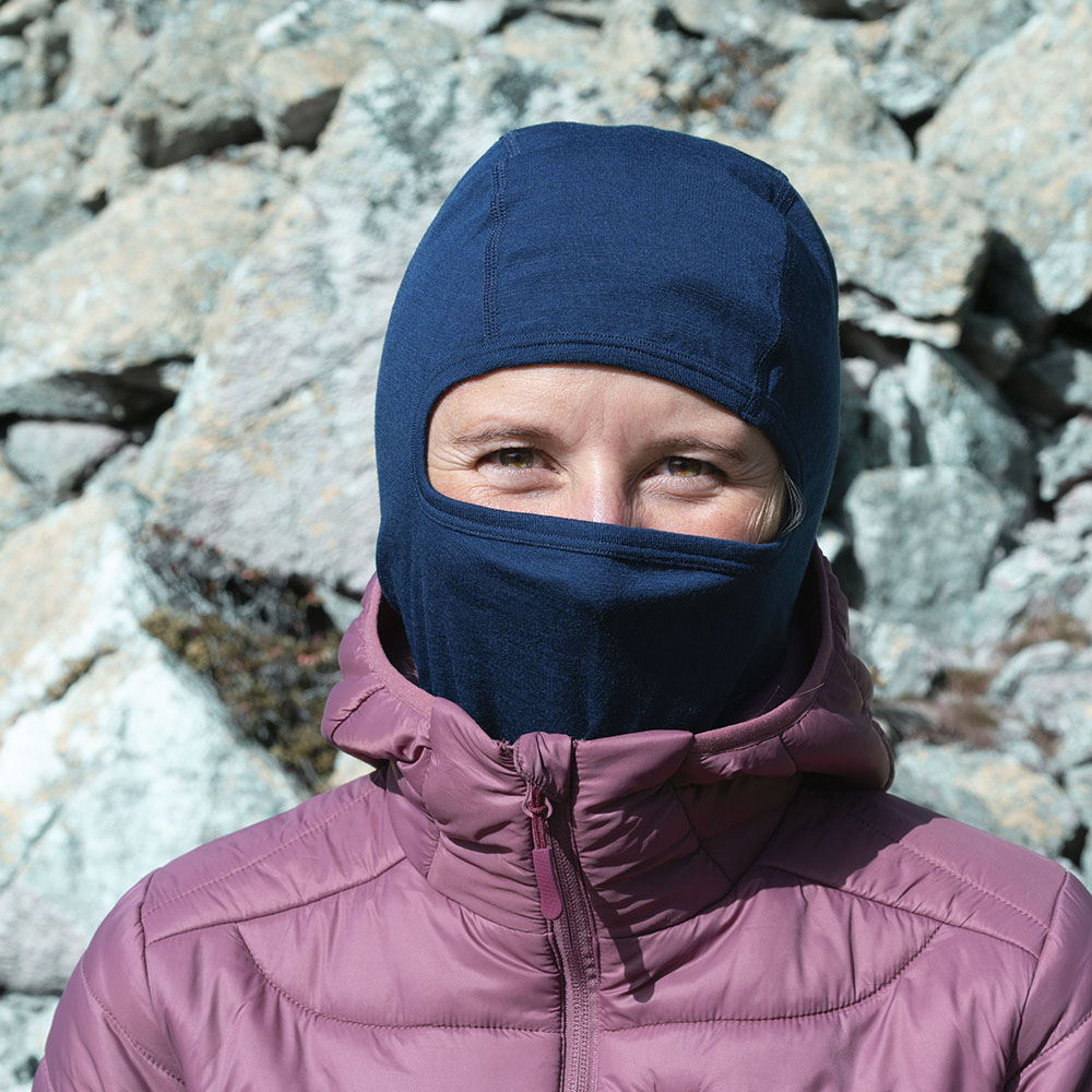 Person in bergiger Umgebung trägt Merino Sturmhaube und Skimaske Herren & Damen, ideal für Outdoor-Aktivitäten. Die Maske bietet ergonomische Passform und Wärme bei kalten Bedingungen.