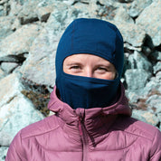 Person in bergiger Umgebung trägt Merino Sturmhaube und Skimaske Herren & Damen, ideal für Outdoor-Aktivitäten. Die Maske bietet ergonomische Passform und Wärme bei kalten Bedingungen.
