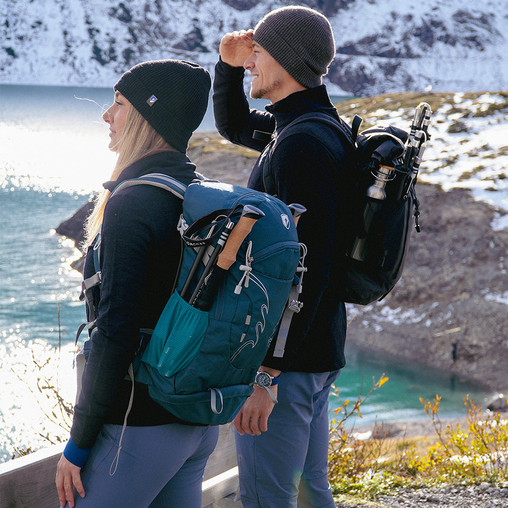 Zwei Wanderer mit dem 30 L Wanderrucksack Herren & Wanderrucksack Damen von Alpin Loacker am Bergsee, ausgestattet für Outdoor-Abenteuer mit Trekkingstöcken und Wasserflasche.