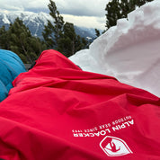 Biwaksack mit Membrane - NEU liegt in verschneiter Berglandschaft, ideal für Outdoor-Abenteuer. Robustes, nachhaltiges Material bietet Schutz vor Wind und Feuchtigkeit.