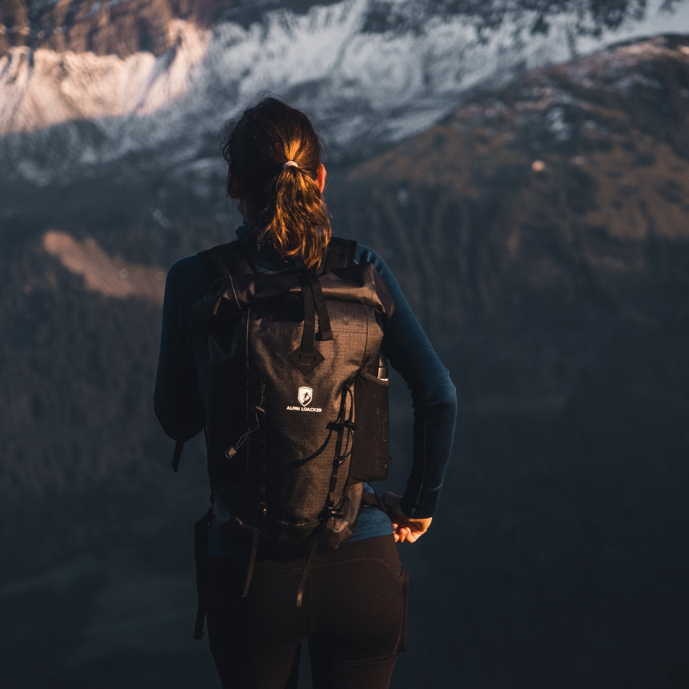 Wanderin mit Alpin Loacker Lotus 25 2.0 Rucksack, blickt auf alpines Panorama. Leichter, wasserdichter Rucksack für Outdoor-Abenteuer.