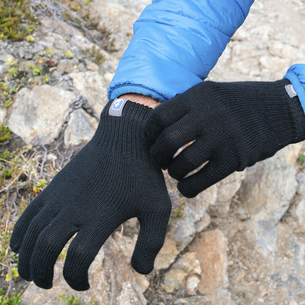 Person im Freien, die Merino Handschuhe Damen & Herren, Classic, anzieht; ideale Wahl für Outdoor-Abenteuer mit Wärme und Geschicklichkeit, erhältlich bei Alpin Loacker.