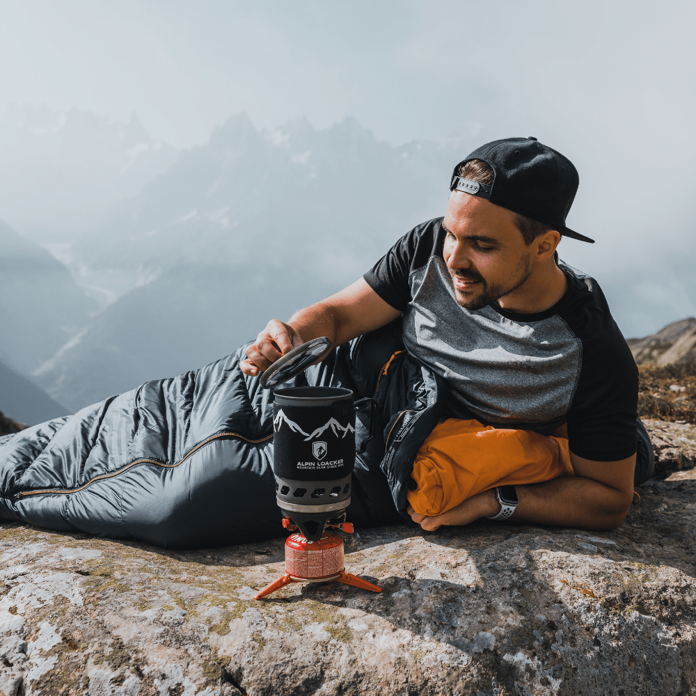 Mann nutzt Alpin Loacker Camping Gaskocher Set auf Berggipfel, umgeben von Nebel. Ideales ultraleichtes Kochset für Outdoor-Abenteuer und schnelle Mahlzeiten.