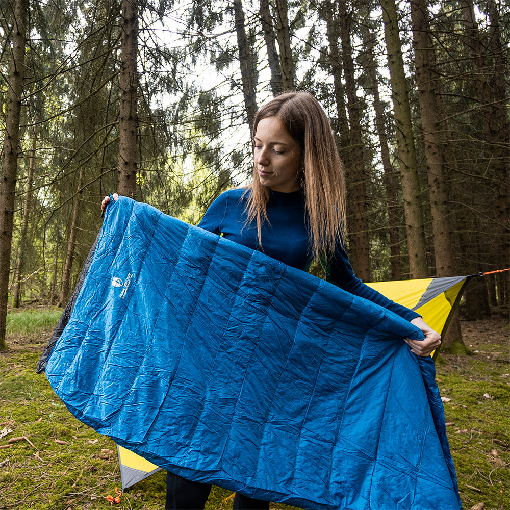 Frau präsentiert den Leichter Sommer Daunenschlafsack in einem Wald, ideal für Outdoor-Abenteuer, zeigt seine ultraleichte und kompakte Bauweise.