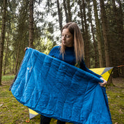 Frau präsentiert den Leichter Sommer Daunenschlafsack in einem Wald, ideal für Outdoor-Abenteuer, zeigt seine ultraleichte und kompakte Bauweise.