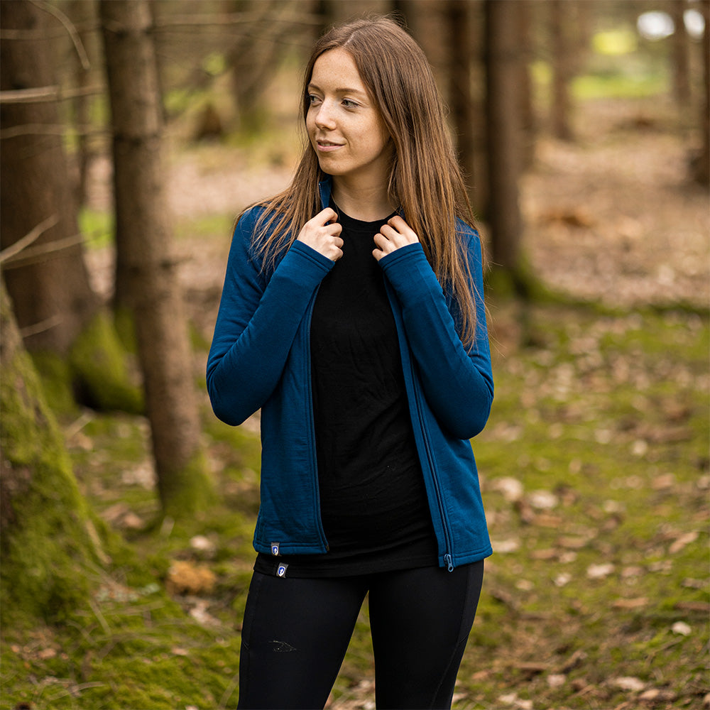 Junge Frau im Wald trägt die Merino Jacke Damen 270 g/m2, ideal für Outdoor-Abenteuer, aus atmungsaktiver Merinowolle, Viskosefasern und Spandex.