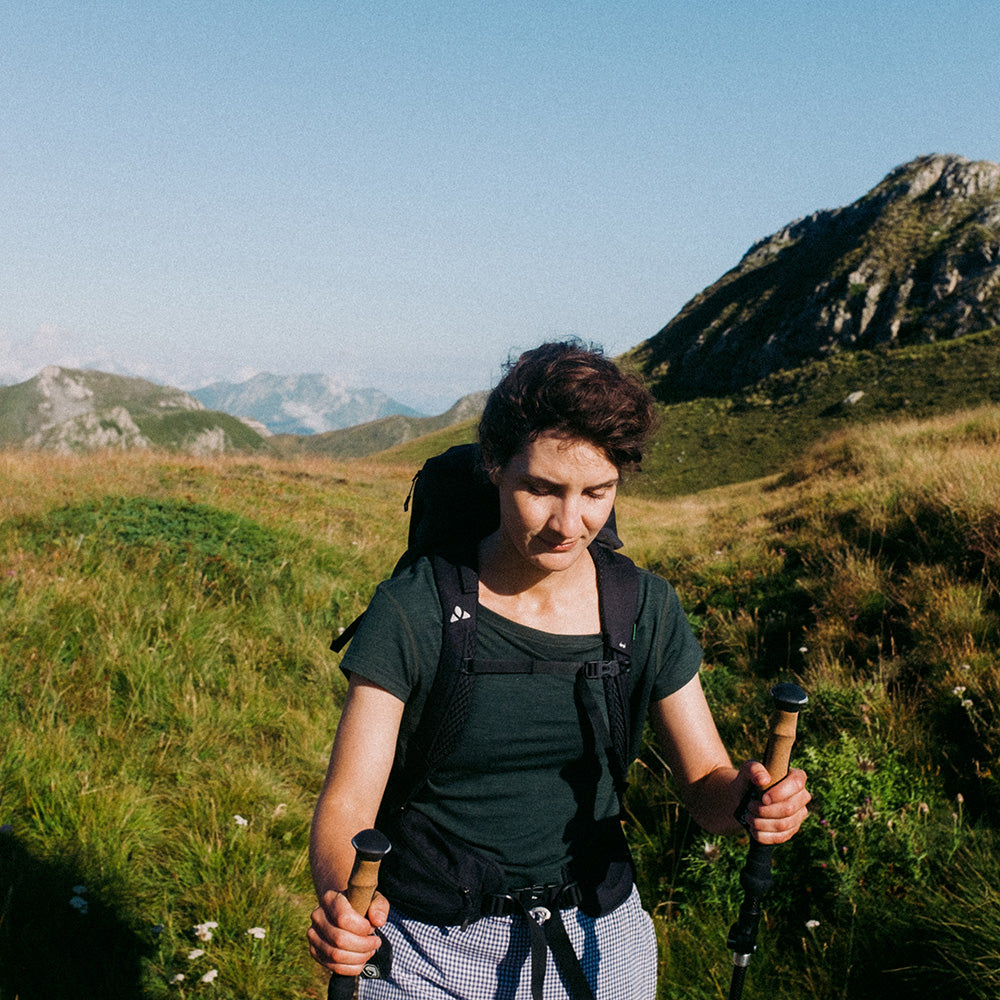 Wanderer mit Trekkingstöcken trägt Merino T-Shirt Damen 150g/m2 im alpinen Gelände, ideal für Outdoor-Abenteuer mit Komfort und Strapazierfähigkeit.