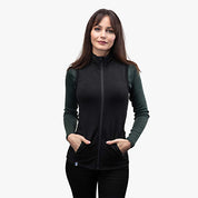 Frau trägt Merino Weste Damen 270g/m2, ärmellos, mit Reißverschluss und Seitentaschen, über dunklem Langarmshirt. Ideal als Midlayer für Outdoor-Aktivitäten.