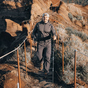Mann wandert mit Alpin Loacker Faltbare Wanderstöcke aus Aluminium auf felsigem Pfad, lächelt in die Kamera, umgeben von rauer, trockener Landschaft.