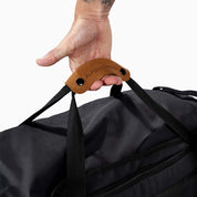 Hand hält die Griffe der Reisetasche, Sporttasche & Duffel Bag von Alpin Loacker mit Ledergriff und sichtbarem Reißverschlussfach. Ideal für Outdoor-Abenteuer.