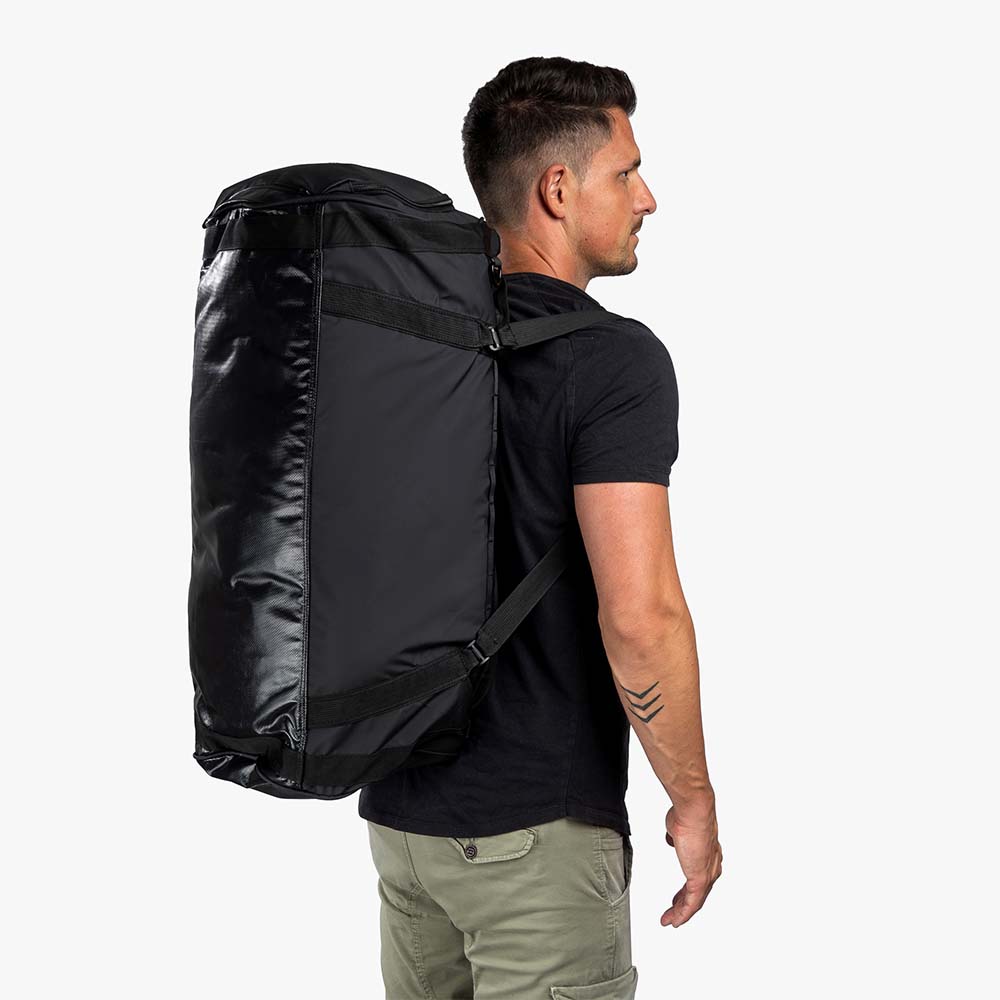 Mann trägt die Reisetasche, Sporttasche & Duffel Bag als Rucksack. Perfekt für Outdoor-Abenteuer mit 70/100 Liter Stauraum und wasserabweisendem Material.