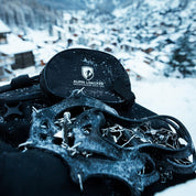 Alpin Loacker Chain Pro 18 Grödel auf schwarzem Tragebeutel, mit Schnee bedeckt, ideal für sicheren Halt auf winterlichen Wegen.