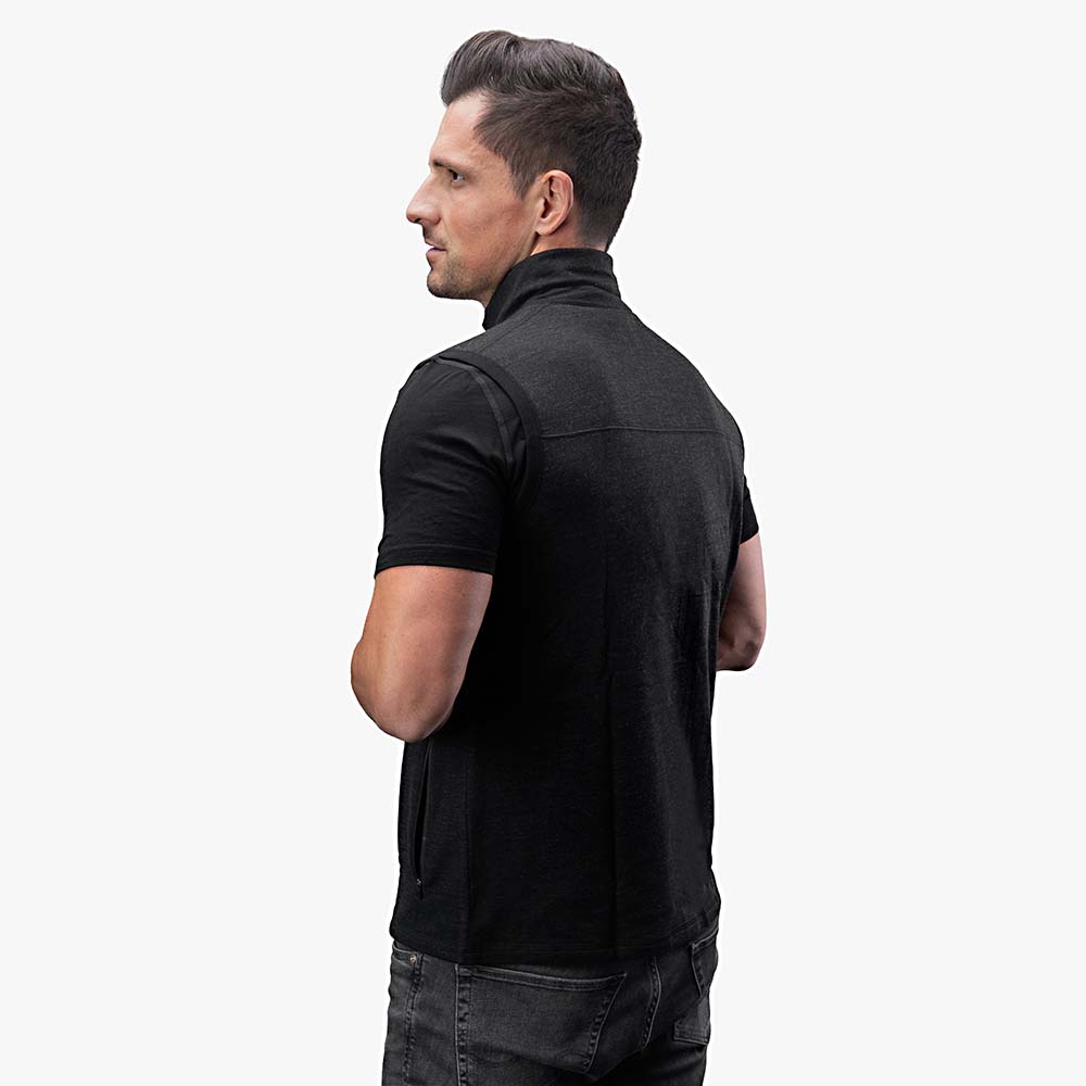 Mann in Merino Weste Herren 270 g/m², schwarzes ärmelloses Design, seitlich gedreht, ideal für Outdoor und Alltag, über schwarzem T-Shirt und Jeans.