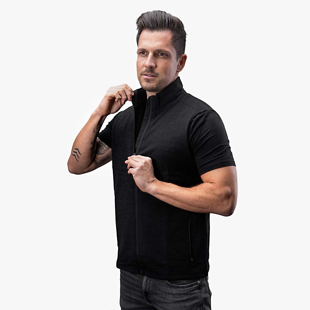 Ein Mann trägt die Merino Weste Herren 270 g/m², zieht den Reißverschluss hoch. Ideal als Midlayer für Outdoor-Aktivitäten und Freizeit.